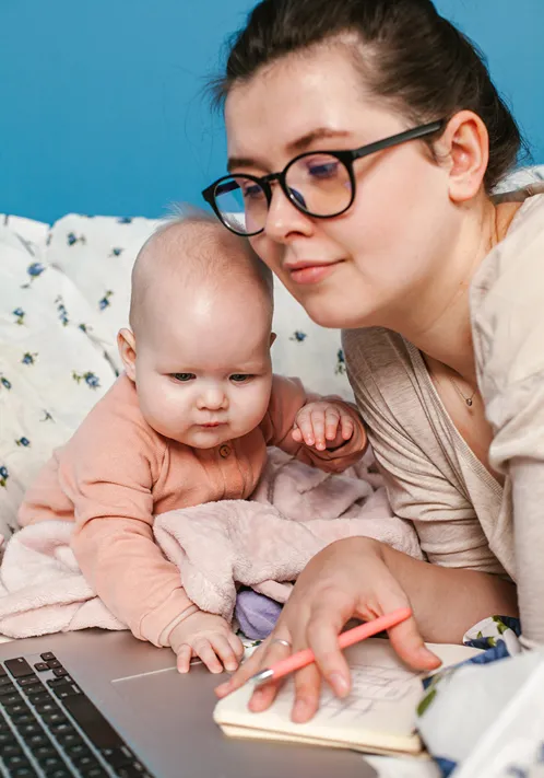 Young mother with baby searching the internet while writing on a notepad.