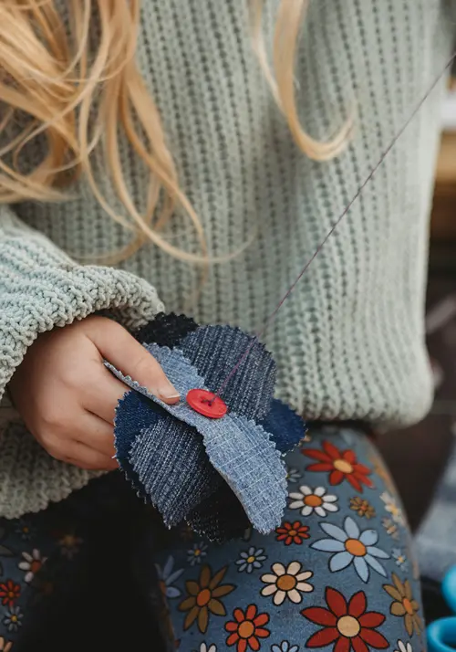 A little girl's hand holds fabric in one hand and pulls thread upward in the other.