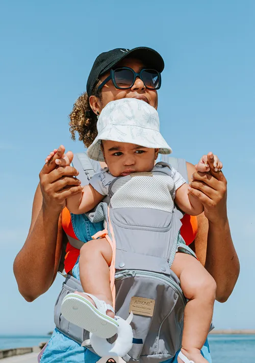Mother with a baby in baby carrier walking outside next to a lake.