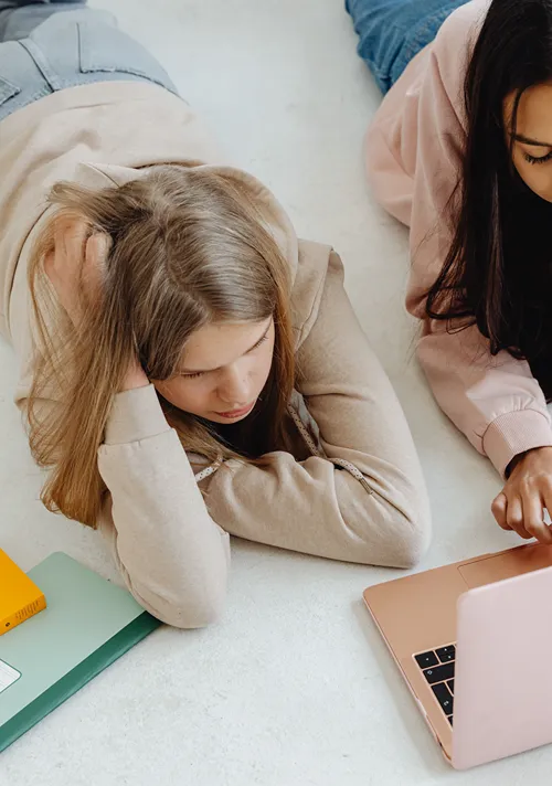 two teens girls on floor with laptop looking at stuff online.