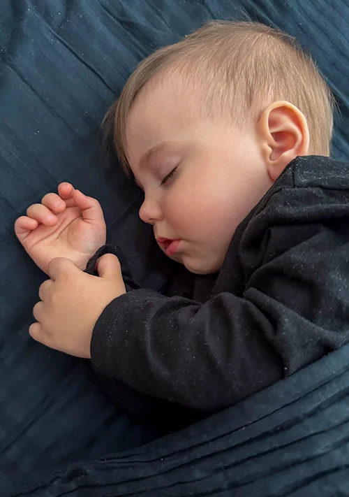 A toddler boy sound asleep in bed.