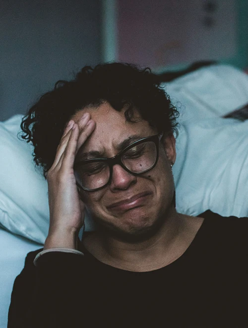 A gravely distraught woman weeping on the floor by her bed.