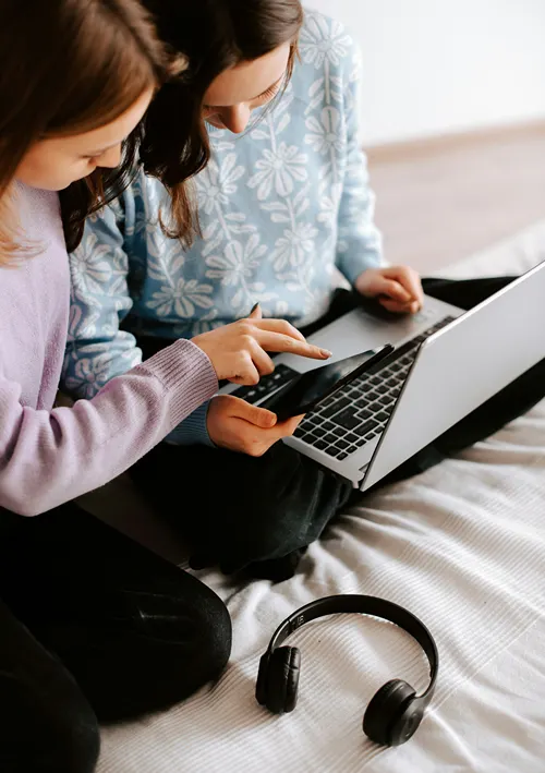 Two young girls on a bed exploring together on a laptop.