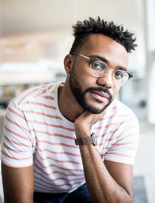 A well dressed stylish man looks up at the camera with a somber demeanor.