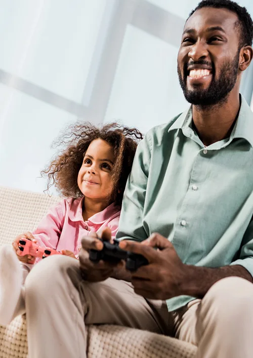 Dad playing a video game with his young daughter on the sofa.