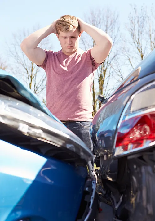 A worried teen holds both hands to his head as he looks at his car in a fender bender.