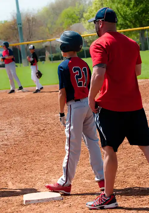 A boy on base while his baseball coach stands behind him.