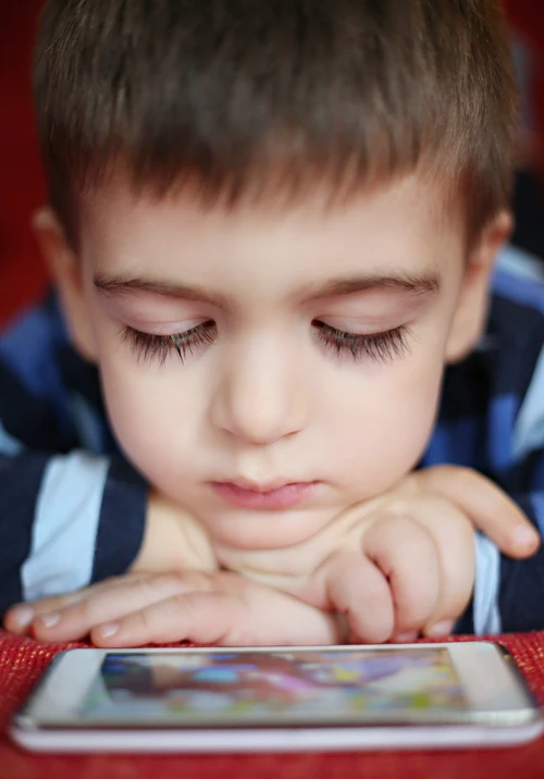 Boy sitting with face close to tablet screen.