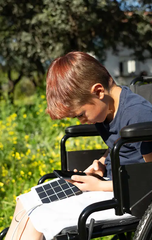 A boy sits outside in a wheelchair using assistive technology connected to his smartphone.