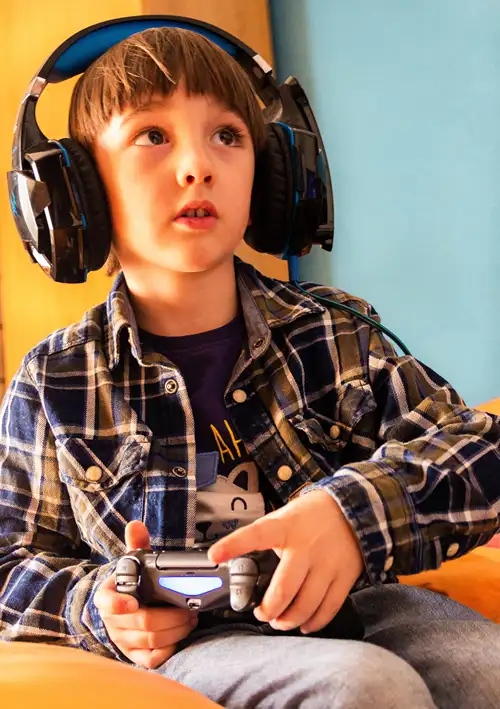 A young boy wearing headphones holding a gaming control.