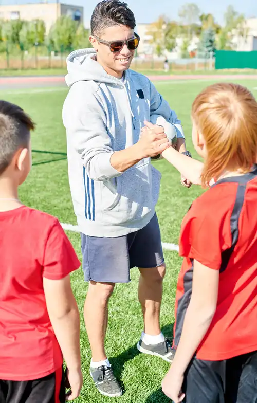 Smiling coach shaking hands with a child on a sports field.