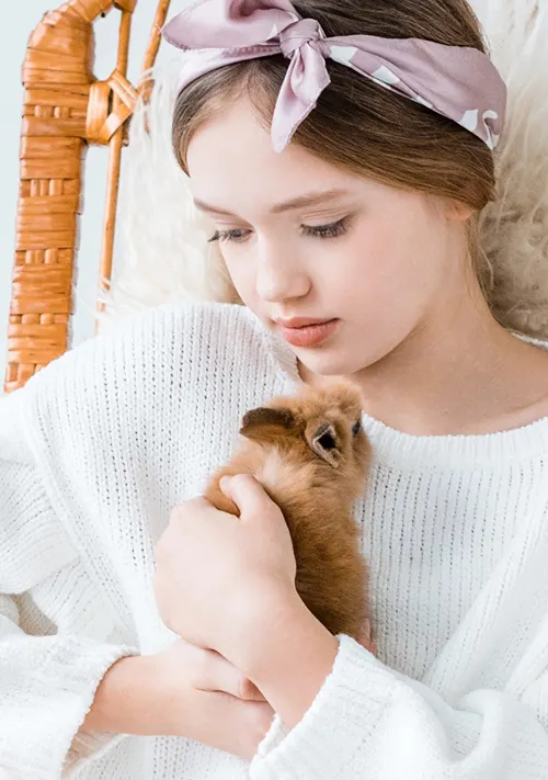 A girl sits in a wicker chair closely sniggles her rabbit.
