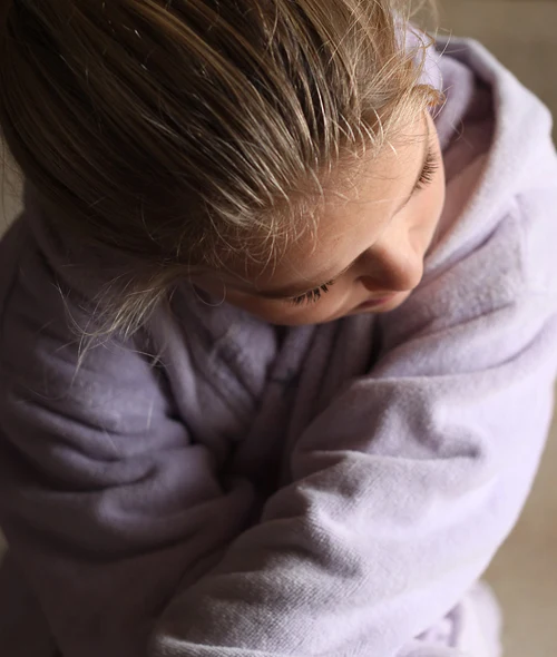 A teen girl hides her face from view as she looks down and crosses one arm over the other.