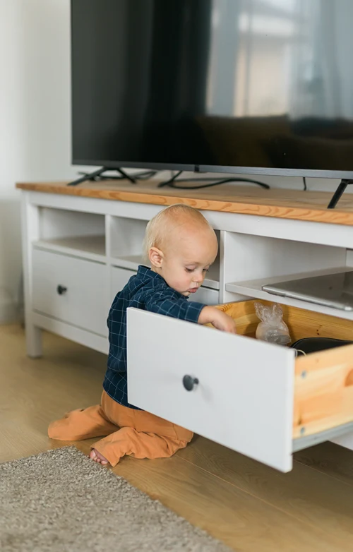 A toddler with his hand in the drawer of a TV stand.