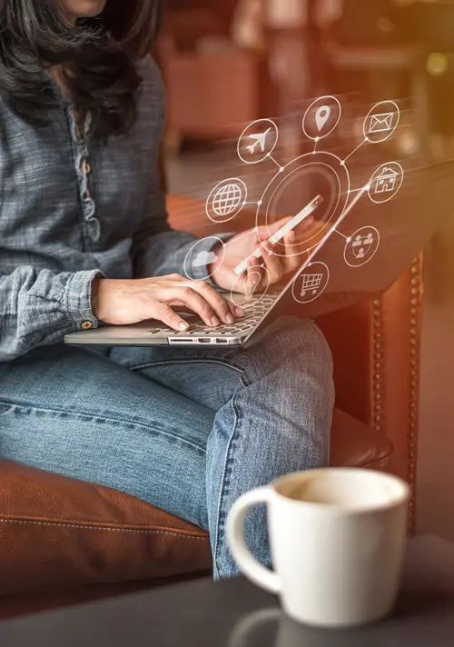 A woman holds her smartphone while using a laptop. Internet related icons are depicted in a circle above.