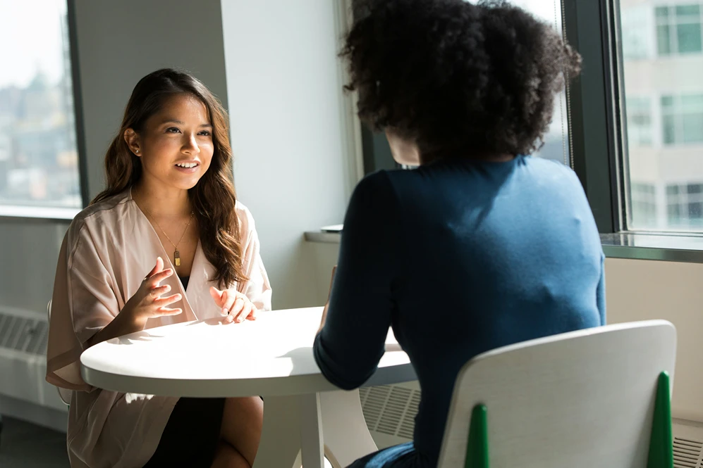 Two women seated at a round table engaged in conversation.